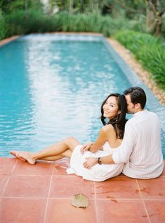 a man and woman sitting next to each other on the ground near a swimming pool