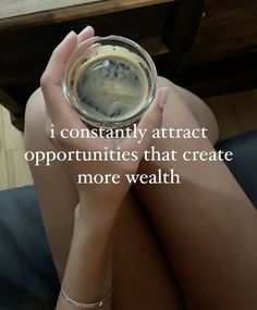 a person holding a glass with liquid in it and the words i constantly attract opportunity that create more wealth