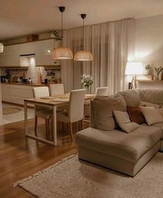 a living room filled with furniture next to a dining room table and two lamps hanging from the ceiling