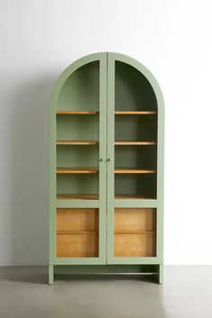 a green bookcase with wooden shelves on the top and bottom, in front of a white wall