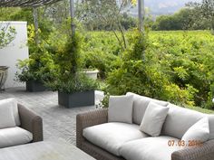 two couches sitting on top of a stone patio next to trees and bushes in the background