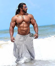 a shirtless man standing in the water at the beach