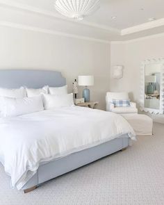 a large white bed sitting in a bedroom next to two chairs and a mirror on the wall