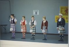 a group of people standing next to each other wearing kilts and dresses in front of a wall