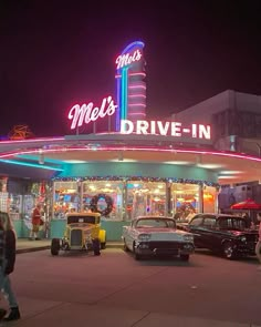 cars parked in front of a drive - in movie theater at night with neon lights