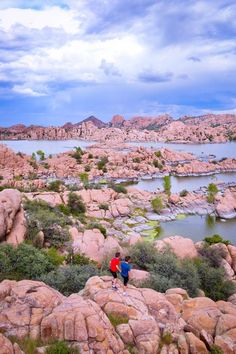 two people standing on top of a rocky hill next to a lake in the desert