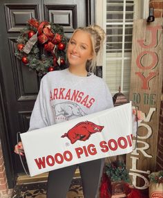 a woman holding a sign in front of a christmas wreath and door with the words, woo pig sooh