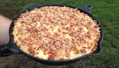 a person holding up a pizza in a cast iron skillet on the grass outside