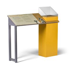 a yellow and silver table with a white box on it's top next to a black metal frame