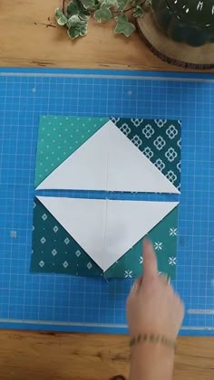 someone is making an origami envelope out of paper on a cutting board next to a potted plant