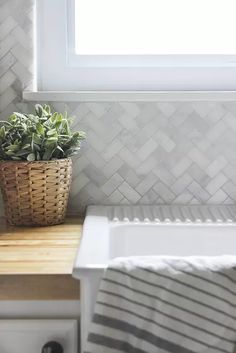 a white sink sitting under a window next to a wooden shelf with a potted plant