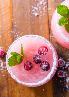 two glasses filled with ice and raspberries on top of a wooden table covered in snow