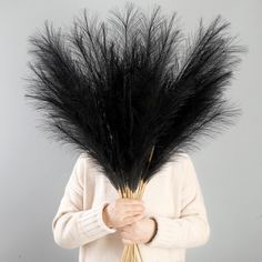 a woman holding a bunch of black feathers on her head and wearing a white sweater