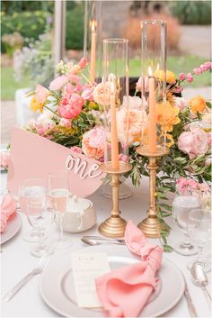 the table is set with pink and yellow flowers in vases, candles, and napkins