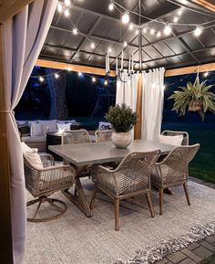 an outdoor dining area is lit up with string lights and white drapes over the table