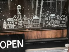 an open sign in front of a window with a cityscape drawn on it