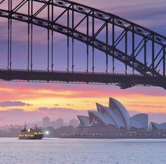 the sydney opera house is lit up at dusk with a boat passing under it and a bridge in the background