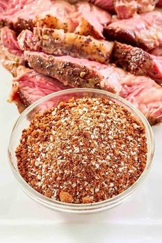 steak seasoning in a glass bowl next to sliced meat on a white counter top