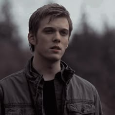 a young man standing in front of trees looking off to the side with his eyes closed