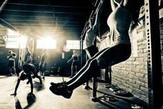 a group of people working out in a gym with one woman doing pull ups on a bar