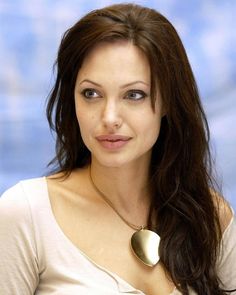 a woman with long brown hair wearing a white shirt and gold heart shaped pendant on her neck