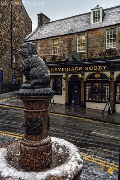 a fountain in front of a building with snow on the ground and buildings around it