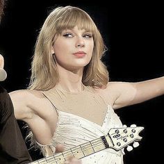 a woman in a white dress holding a guitar and pointing to the side with her right hand