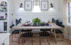 a dining room table with chairs and pictures on the wall above it, along with potted plants