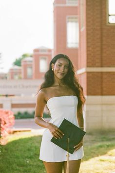 a woman in a short white dress holding a black folder and posing for the camera