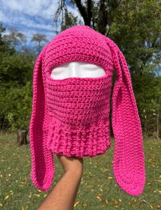 a person is holding up a pink crocheted hat with a bunny ears on it