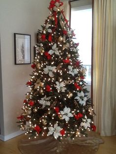 a decorated christmas tree with red, white and silver decorations in a living room area