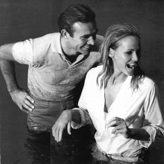 black and white photograph of man and woman laughing in water with one holding his arm around the other's shoulder