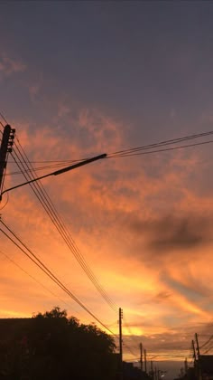 the sun is setting behind power lines and telephone poles in front of some houses with trees