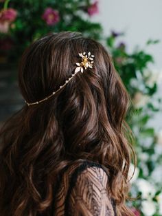 a woman with long brown hair wearing a gold flower headpiece in front of flowers