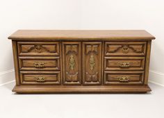 an old wooden dresser with many drawers and knobs on the doors is against a white wall