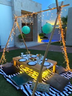 a table set up with lights and pillows on the grass in front of a house