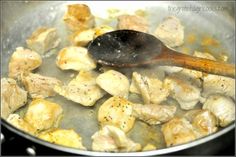 chicken and potatoes cooking in a pan with a wooden spoon