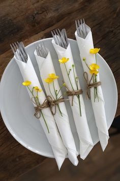 four napkins tied with twine and yellow flowers on a white plate next to silverware