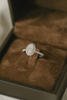 an engagement ring sits in a box on top of a brown velvet cushioned surface