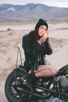 a woman sitting on top of a motorcycle eating an ice cream cone with mountains in the background