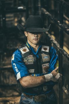 a man with his arms crossed wearing a cowboy hat and blue shirt is standing in front of some stairs