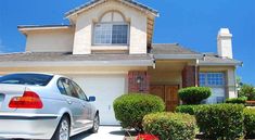 a white car parked in front of a house with bushes and shrubs around the driveway