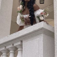 a woman with long black hair wearing a white dress and holding flowers in her hand