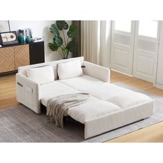 a white sectional sofa sitting on top of a wooden floor next to a plant in a living room