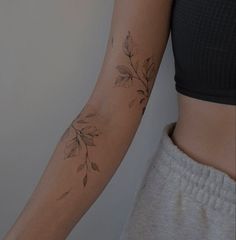 a woman's arm with leaves on it and a tattoo design on the wrist