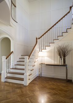 a white staircase with wood flooring next to a table and vase on top of it