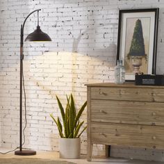 a living room with a white brick wall and floor lamp next to a wooden dresser