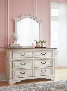 a white dresser sitting in front of a pink wall with a mirror on top of it