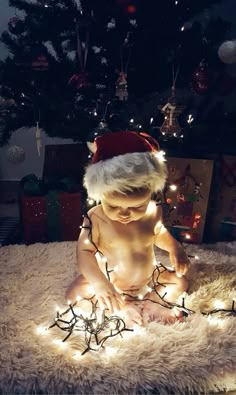 a baby sitting on the floor with christmas lights around him