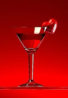 a martini glass with an apple on the rim in front of a bright red background